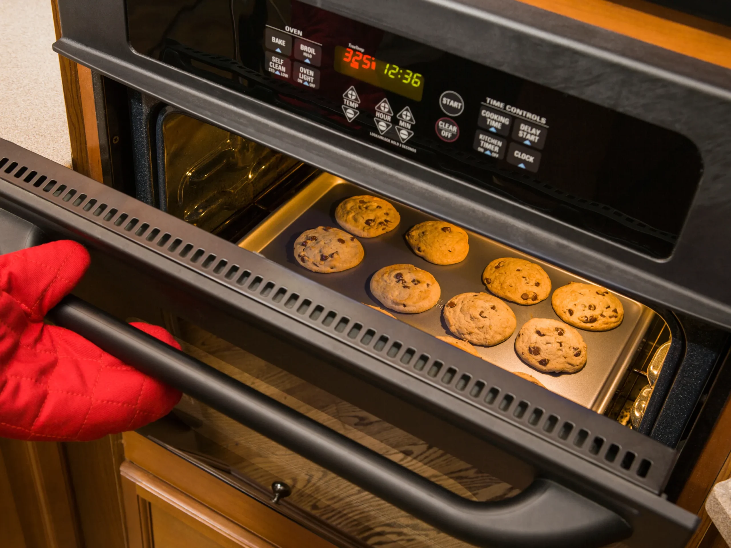 oven mitt opening up an oven with cookies in it